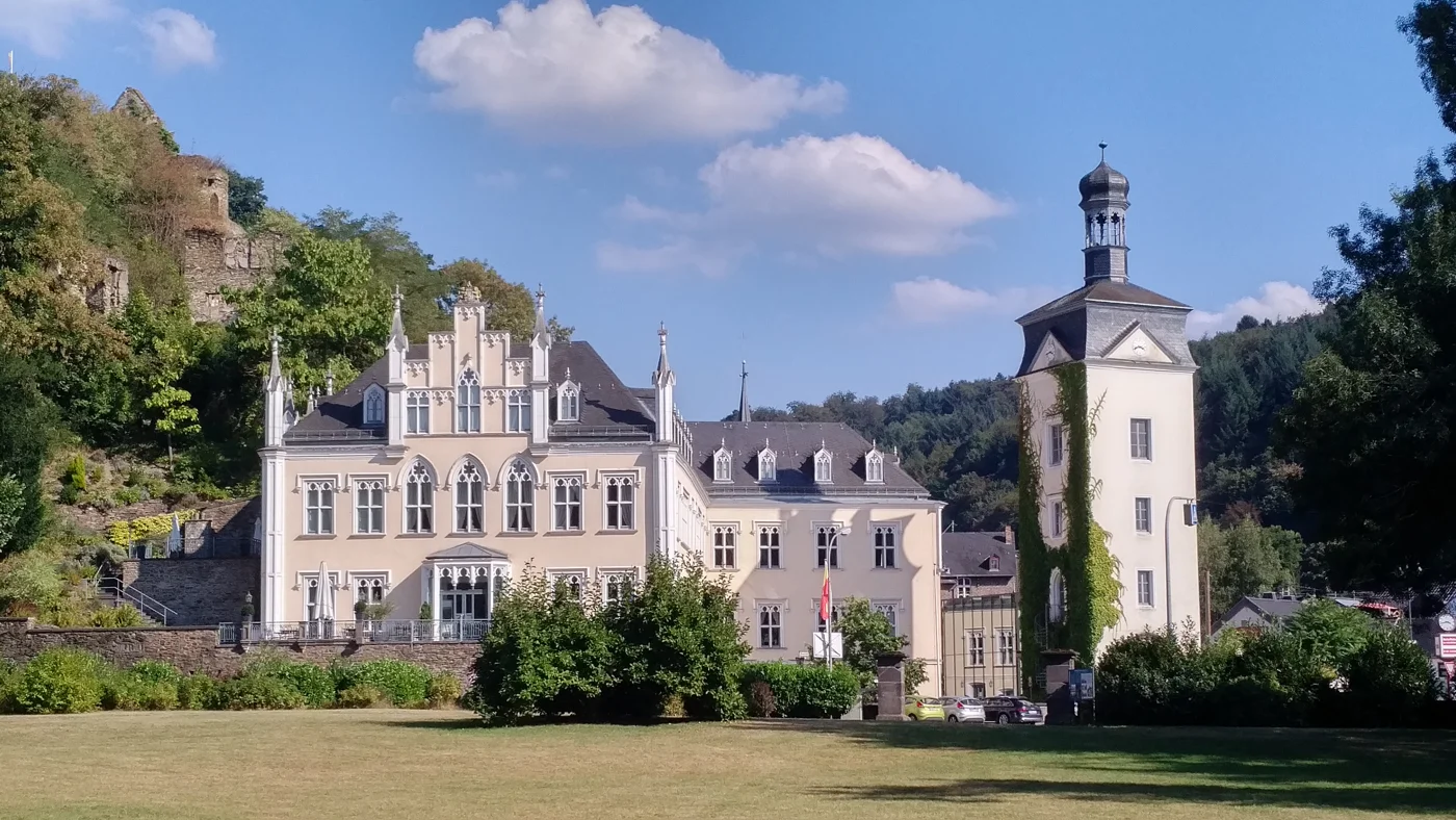 Schloss Sayn im Tal mit der bewaldeten Burgruine Sayn links darüber